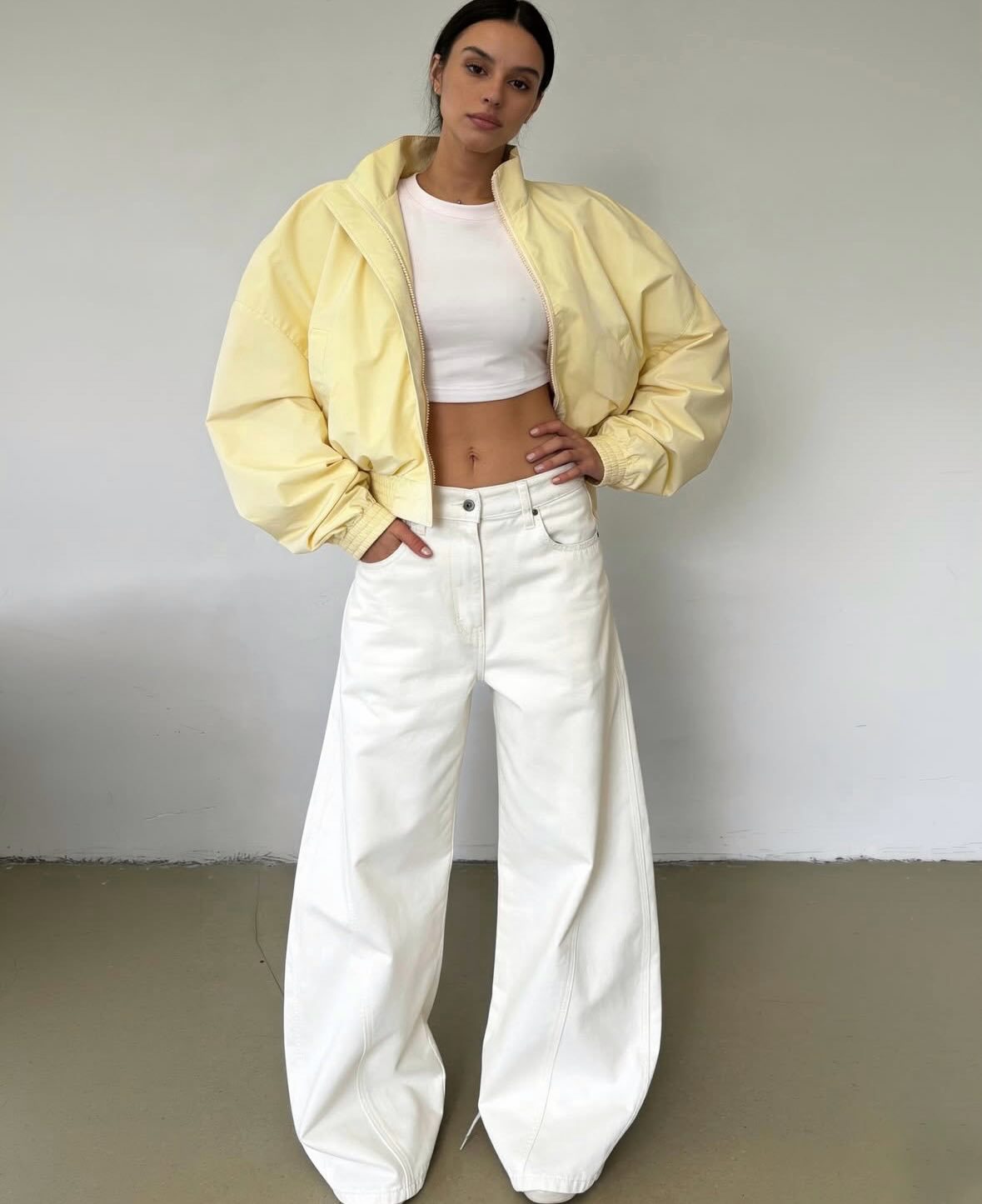 Pale yellow cropped bomber jacket, front view on model, open, over white crop top and white wide-leg trousers
