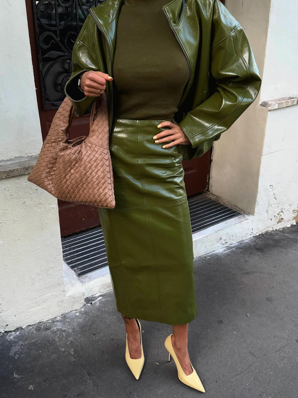 Faux-leather jacket and midi skirt co-ord set in olive green, front view on model, hand on hip, brown bag, urban background