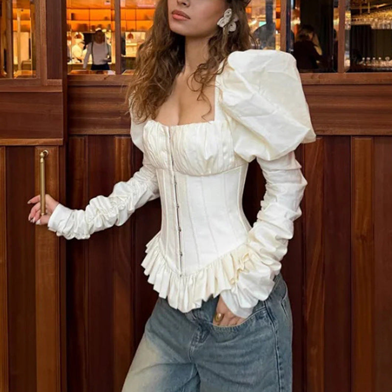 White square-neck corset top with puff sleeves and peplum hem, side view on model near wooden paneling