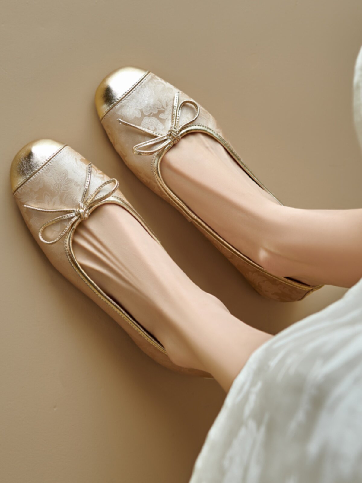 Gold floral ballet flats with metallic toe cap and bow, worn on feet, flat lay view