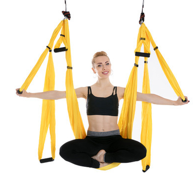 Yellow aerial yoga hammock with handles, model sitting cross-legged in the sling