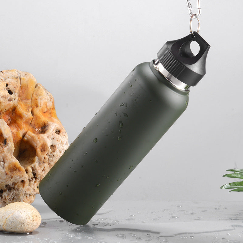 Olive green stainless steel vacuum bottle with carabiner lid, angled side view, resting on rock with water droplets
