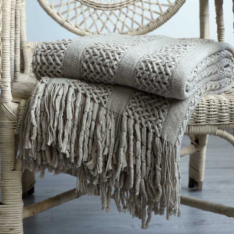 Chunky lattice knit throw in beige with tassels, folded on a wicker chair, front view