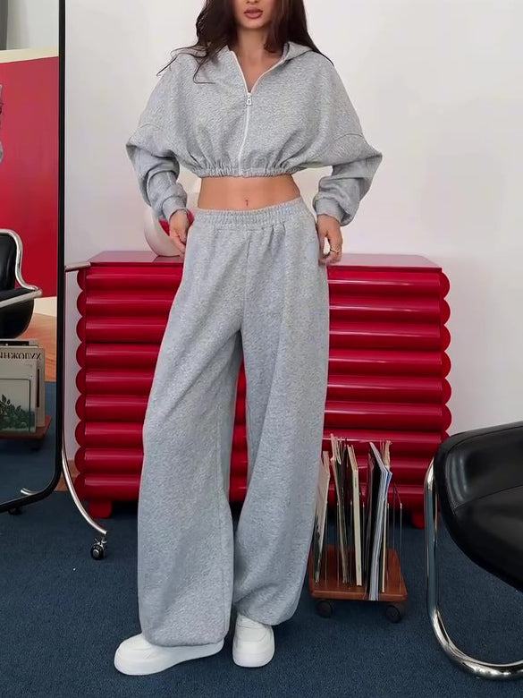 Grey corset top, cropped hoodie and wide-leg trousers set on model, front view, hands on hips, red cabinet background