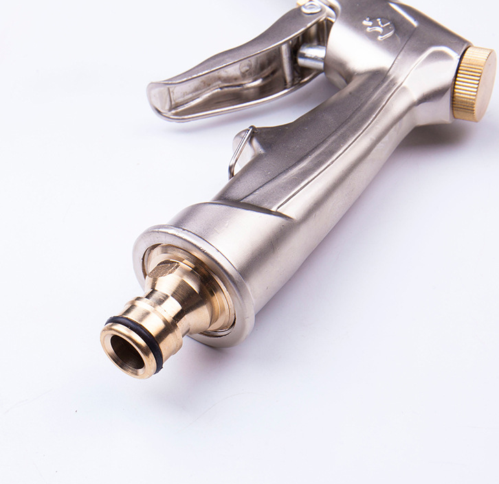 Close-up of garden hose spray gun, showing brass-tone connector and trigger mechanism, silver body, white background