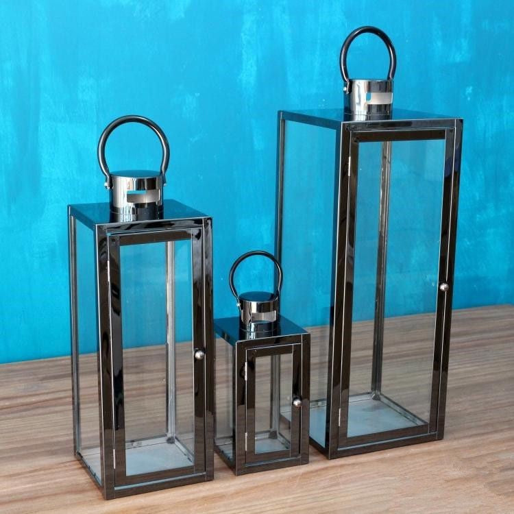 Drie zilverkleurige lantaarns met glas, leeg, op een tafel voor een blauwe muur