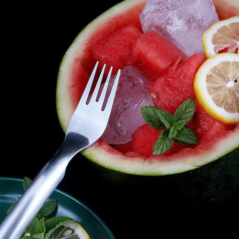 2-in-1 stainless steel watermelon fork and cutter, silver, resting on a watermelon bowl with ice and lemon, side view