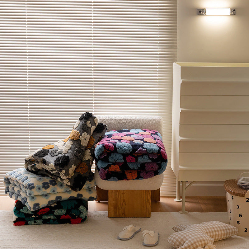Double-Layer Tufted Flower Blanket in multiple patterns stacked on a stool and floor near a window with blinds and a storage