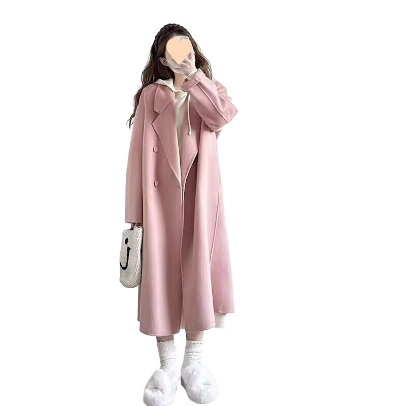 Long oversized double-breasted coat in pink, worn by a model against white background, front view with white shoes