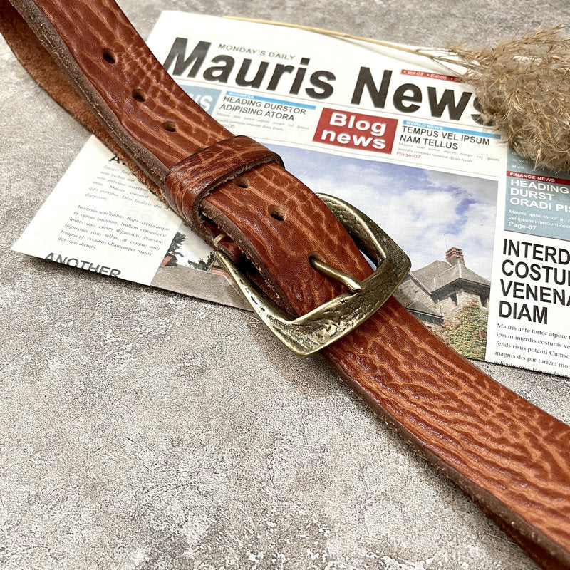 Leather belt tan colour, bronze-tone buckle, placed on newspaper, flat lay