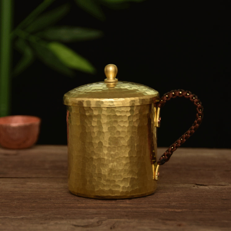 Hammered brass mug with lid on, front view on wooden surface