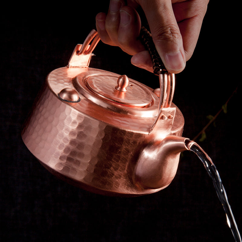 Copper teapot in use, being poured by hand, showing spout and handle detail