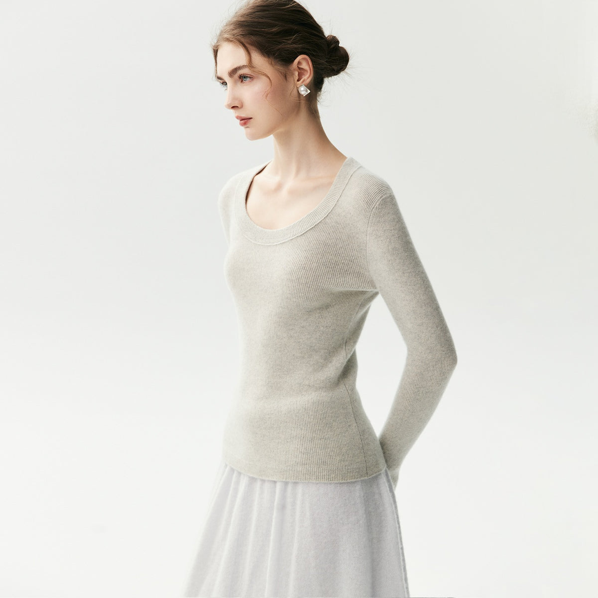 Lichtgrijze geribde cashmere trui met U-hals op een model, zijaanzicht met witte rok