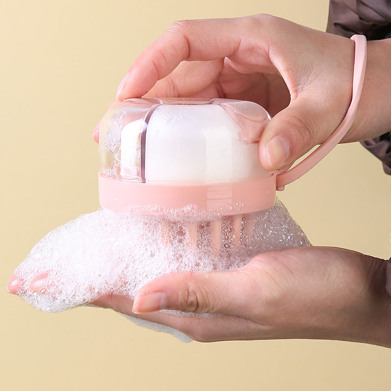 Pink shampoo brush with dispenser, held in one hand with foam coming out of the teeth onto the other palm
