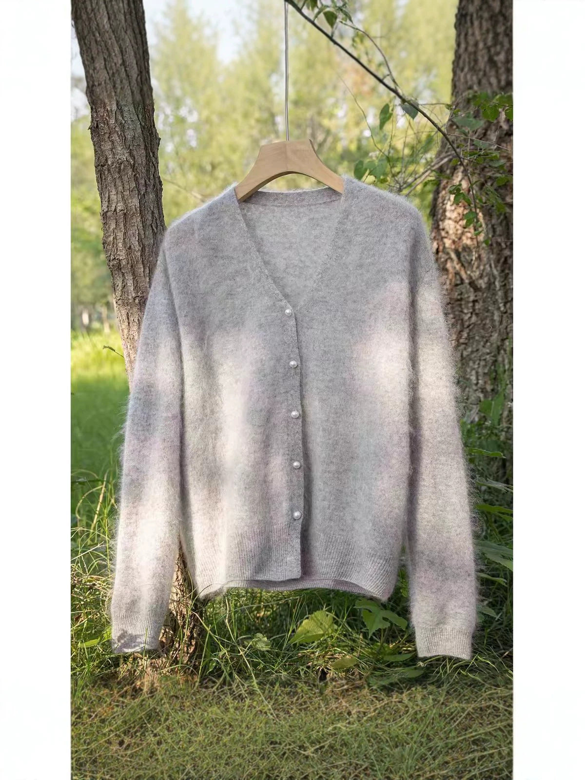 Grijs wollen vest dames met parelachtige knopen, geborsteld, aan een hanger tussen twee bomen
