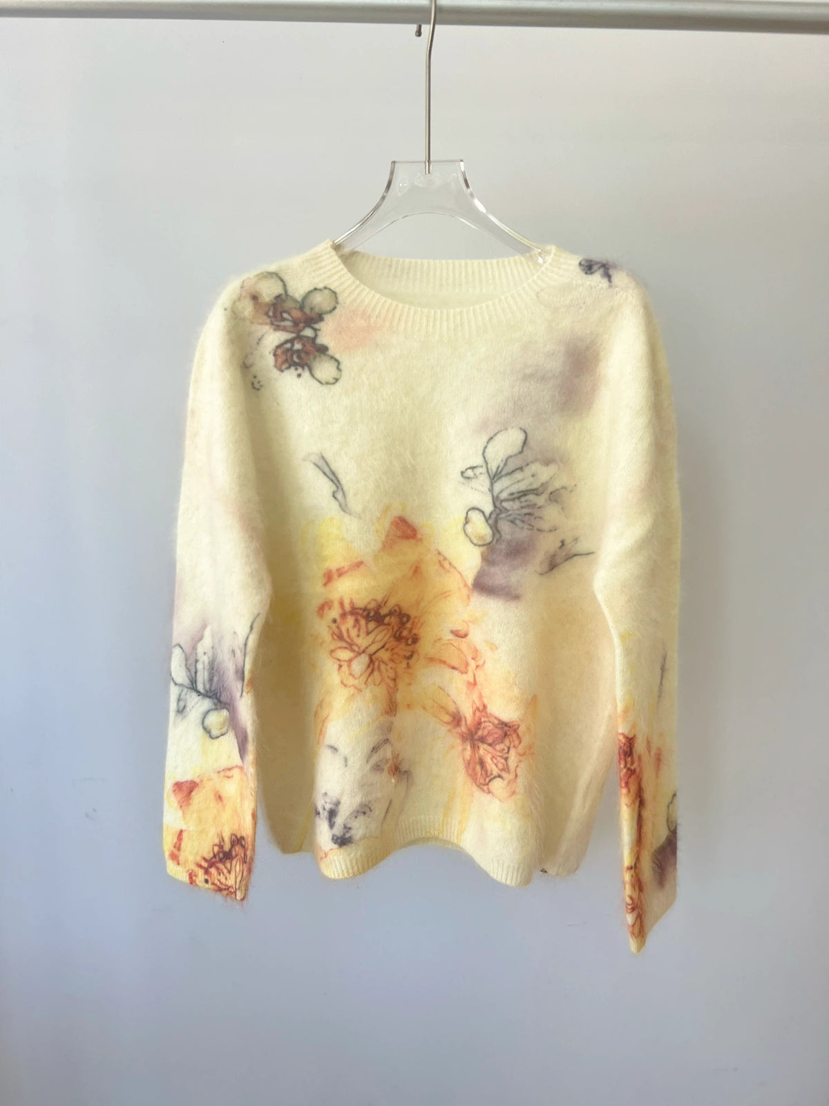 Geborstelde trui met oranje en gele verloop bloemenprint op een lichtgele basis, hangend aan een hanger
