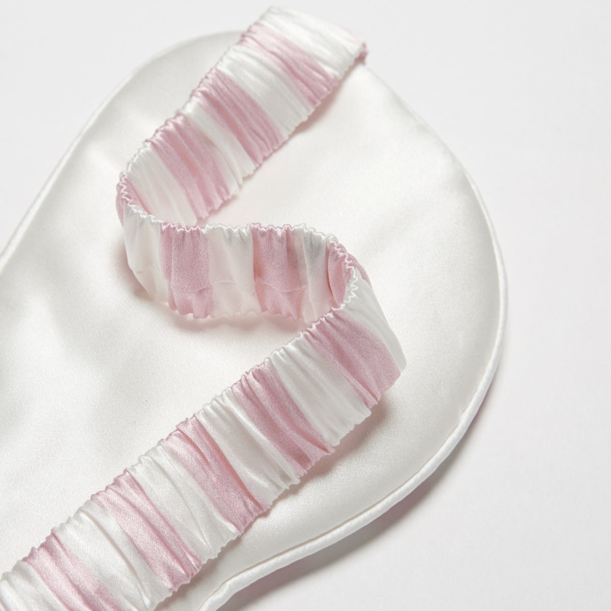 Achterkant van een roze gestreept zijden slaapmasker met de geplooid elastische band in dezelfde stof