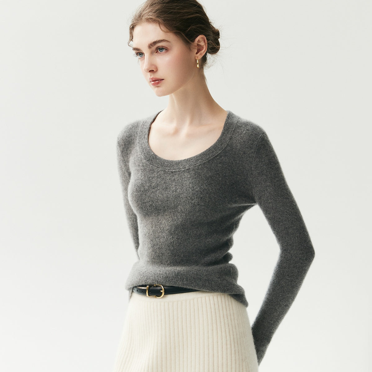 Antraciet geribde cashmere trui met U-hals op een model, zicht op driekwart met cream rok en riem