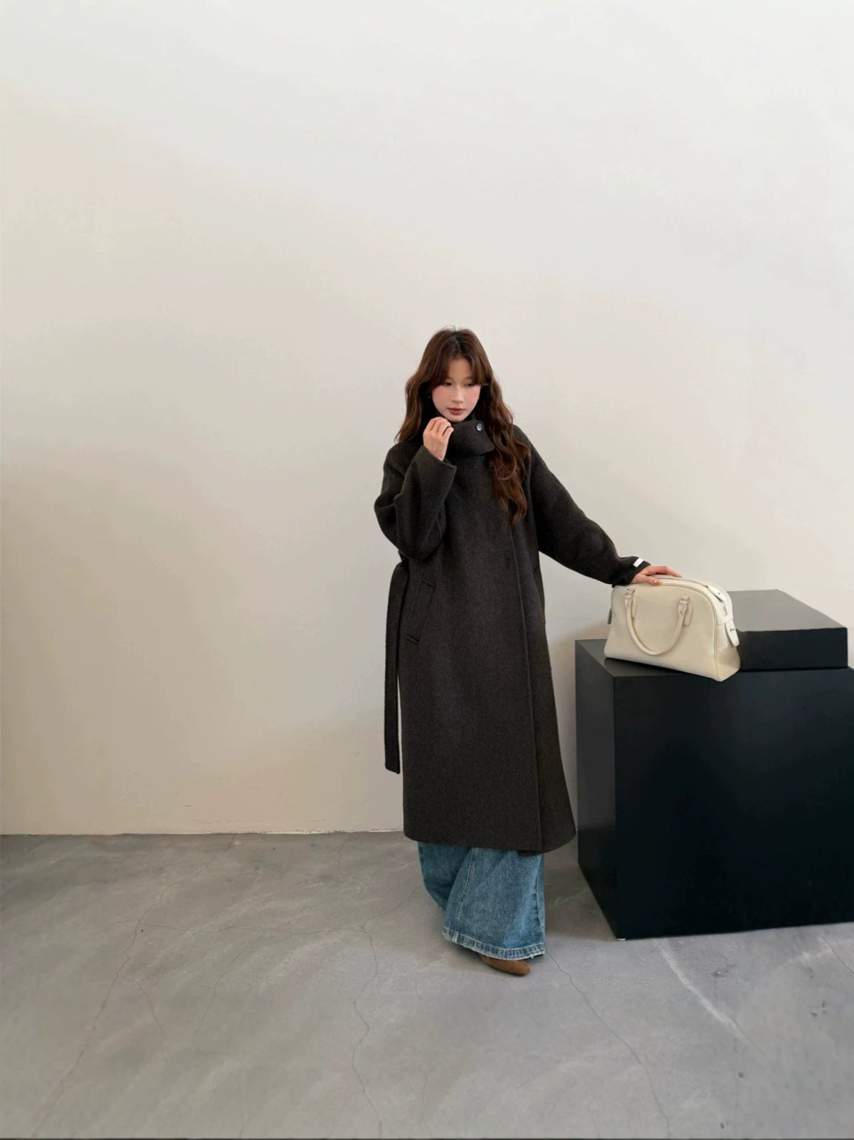 Charcoal grey long wool coat, full front view on model next to a black plinth
