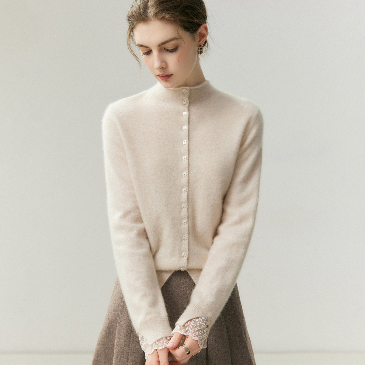 Crème kasjmier vest, model die naar beneden kijkt met in elkaar gevouwen handen om het detail van de kantmanchet te laten zien