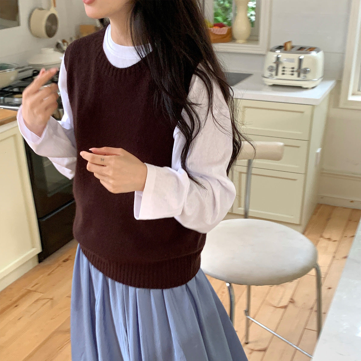 Chocoladebruine gebreide gilet over een witte top met lange mouwen en lichtblauwe rok