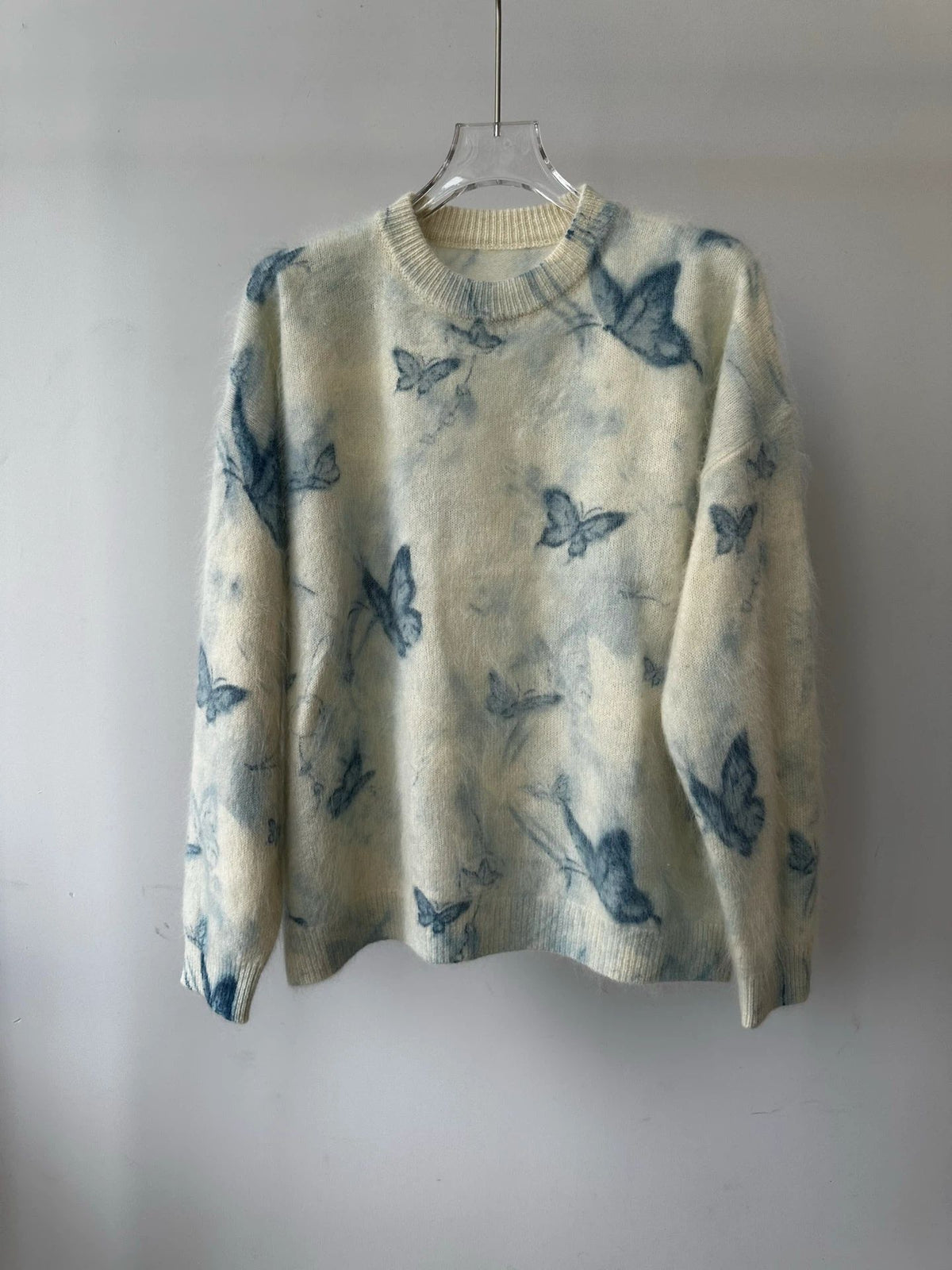 Geborstelde wollen trui met blauwe vlinderprint op een lichtblauwe basis, hangend aan een hanger