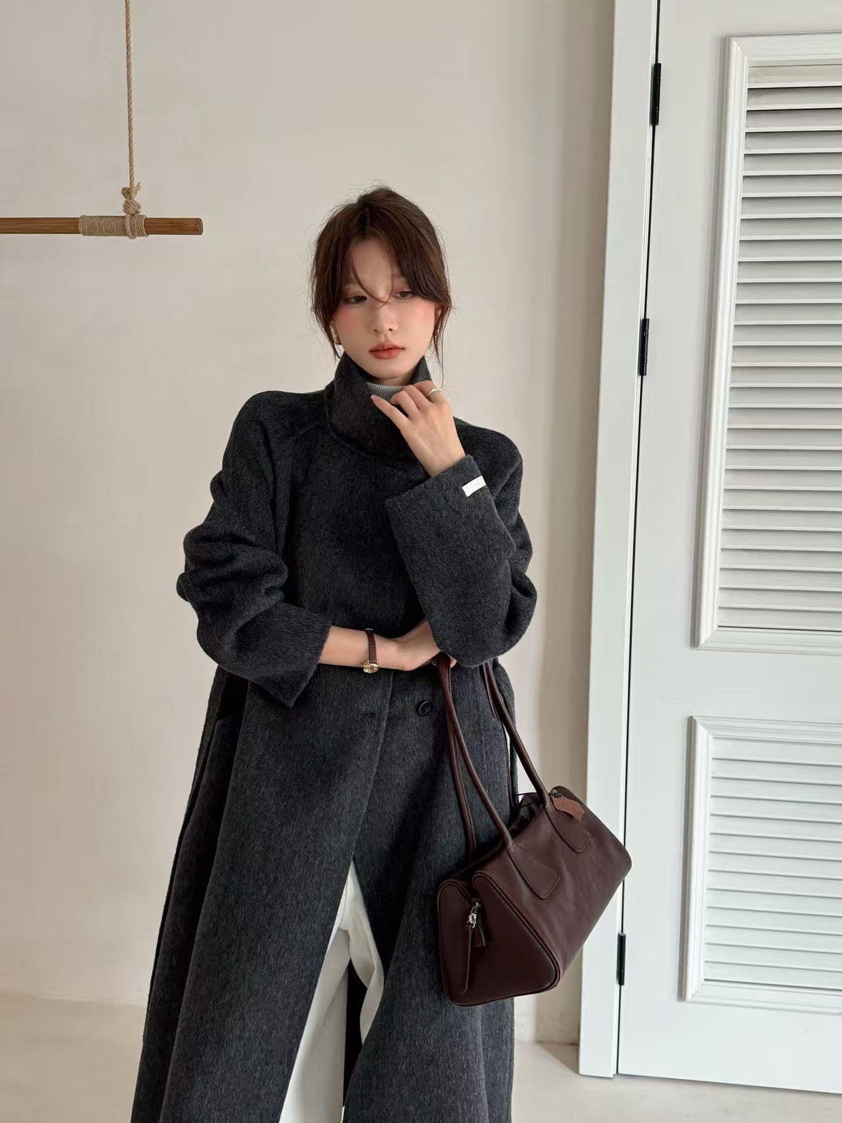 Charcoal grey wool coat with stand collar, front view on model holding a brown bag