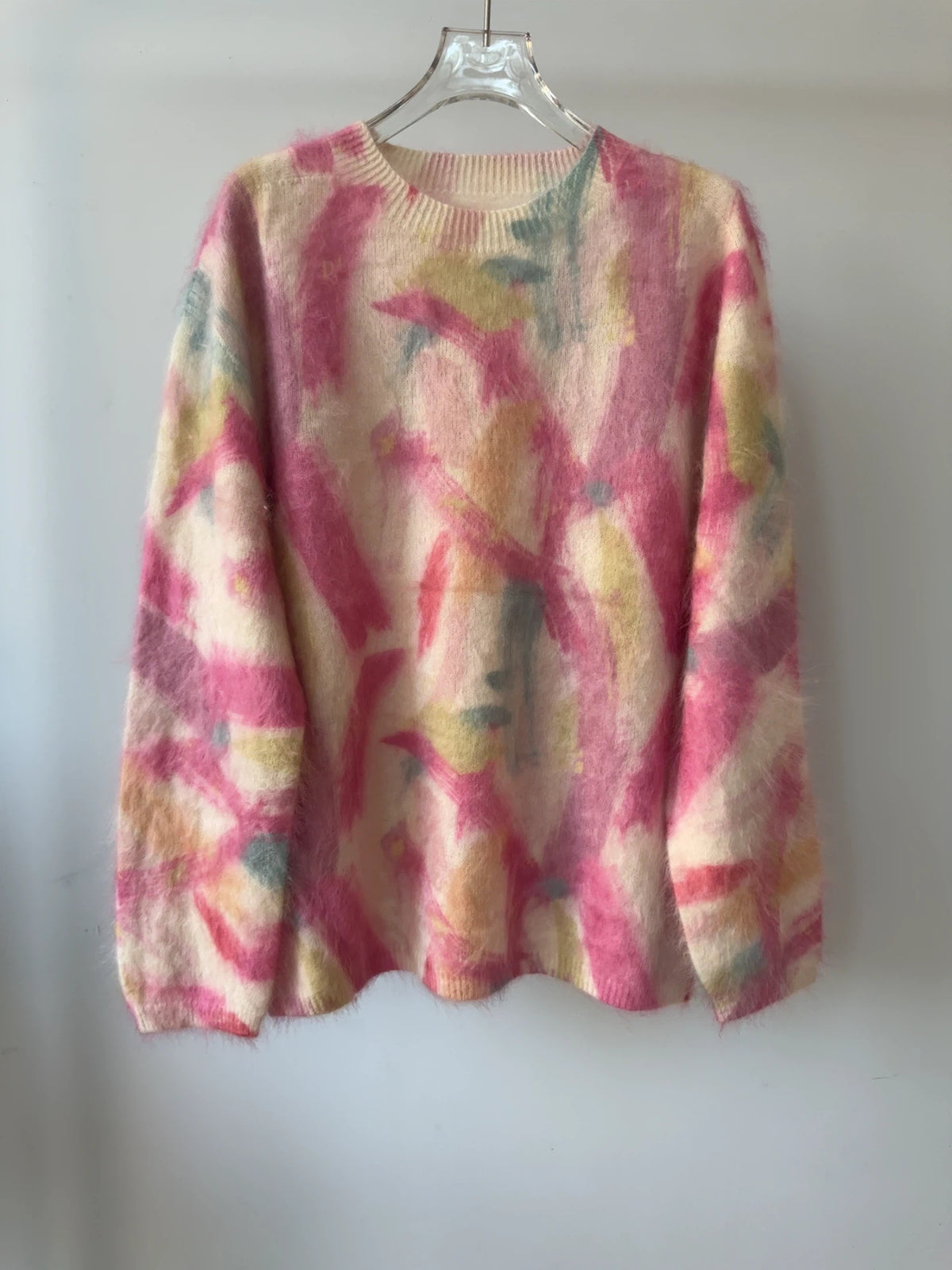 Geborstelde trui met roze en gele abstracte vluchtige print op een crèmekleurige basis, hangend aan een hanger