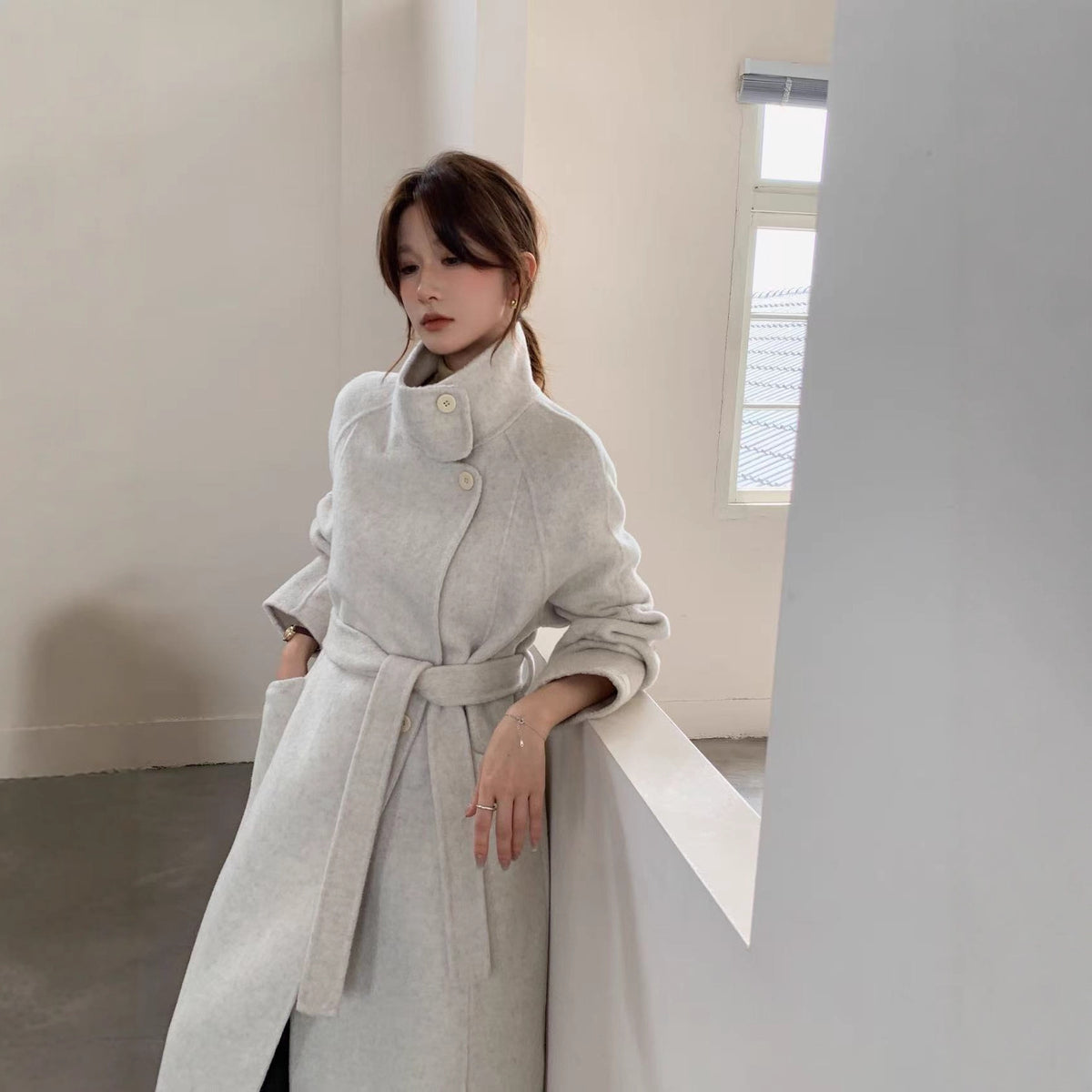 Light grey double-faced wool coat, front view on model leaning on a white railing