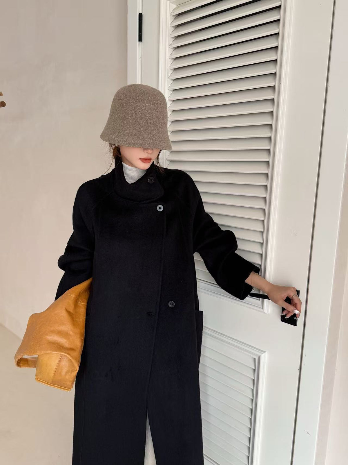 Black wool coat with stand collar, front view on model wearing a beige bucket hat