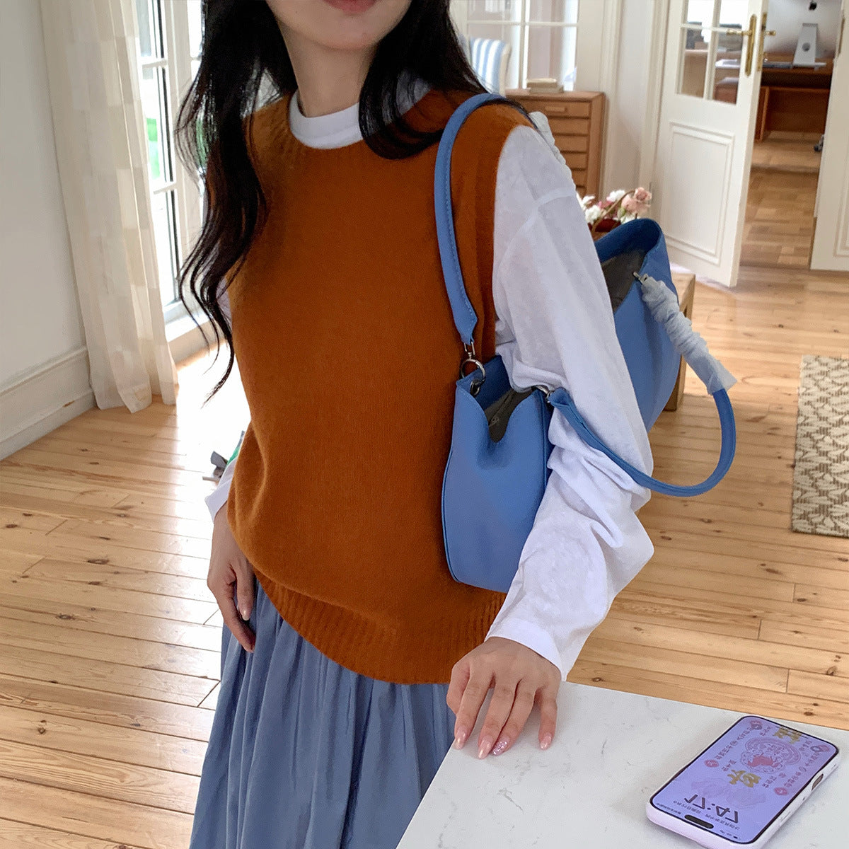 Pompoenoranje gebreide gilet met ronde hals, gedragen over een wit overhemd en blauwe geplisseerde rok