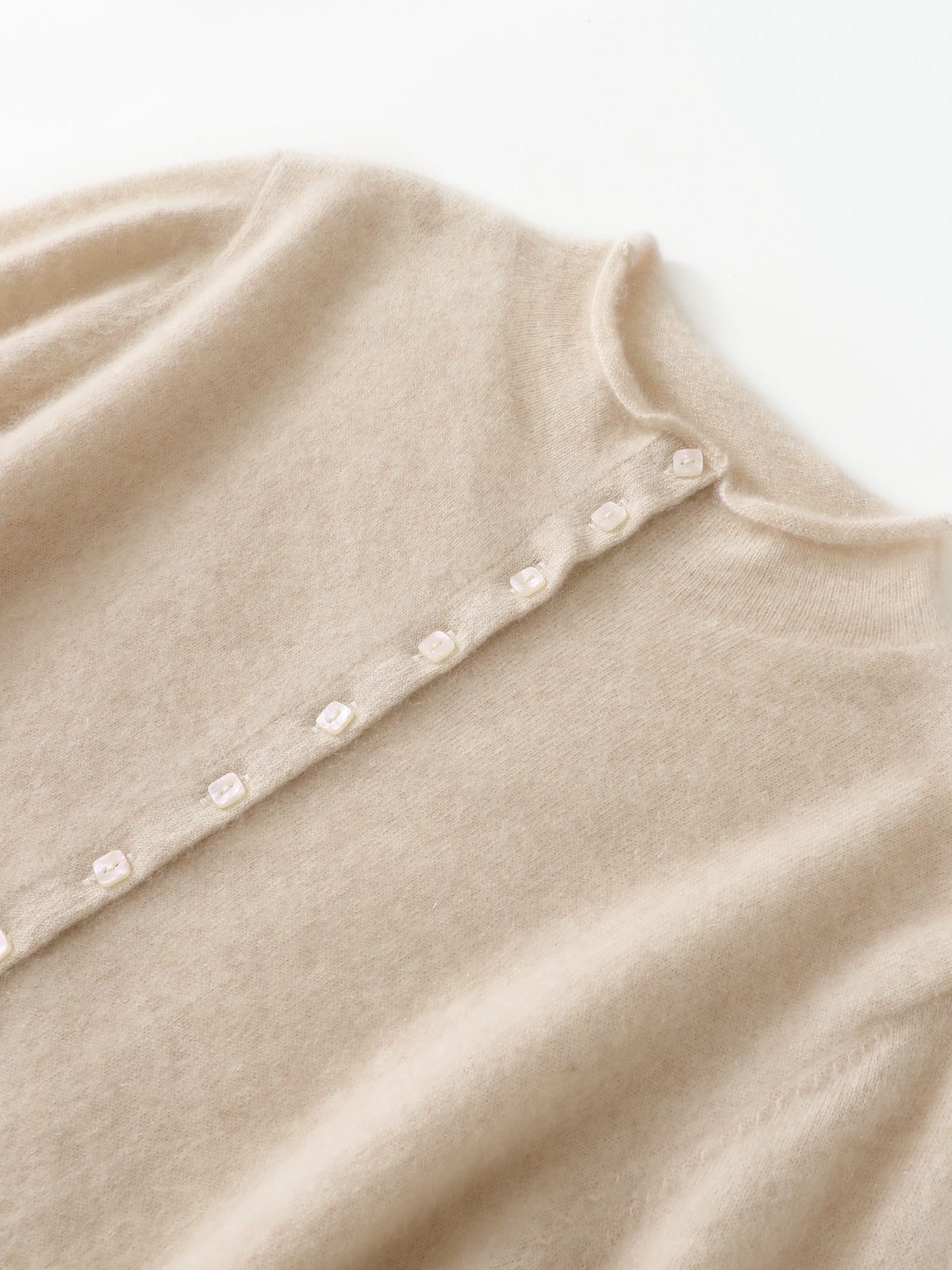 Close-up van de opstaande rolkraag en de rij kleine ronde knopen van een crème kasjmier vest