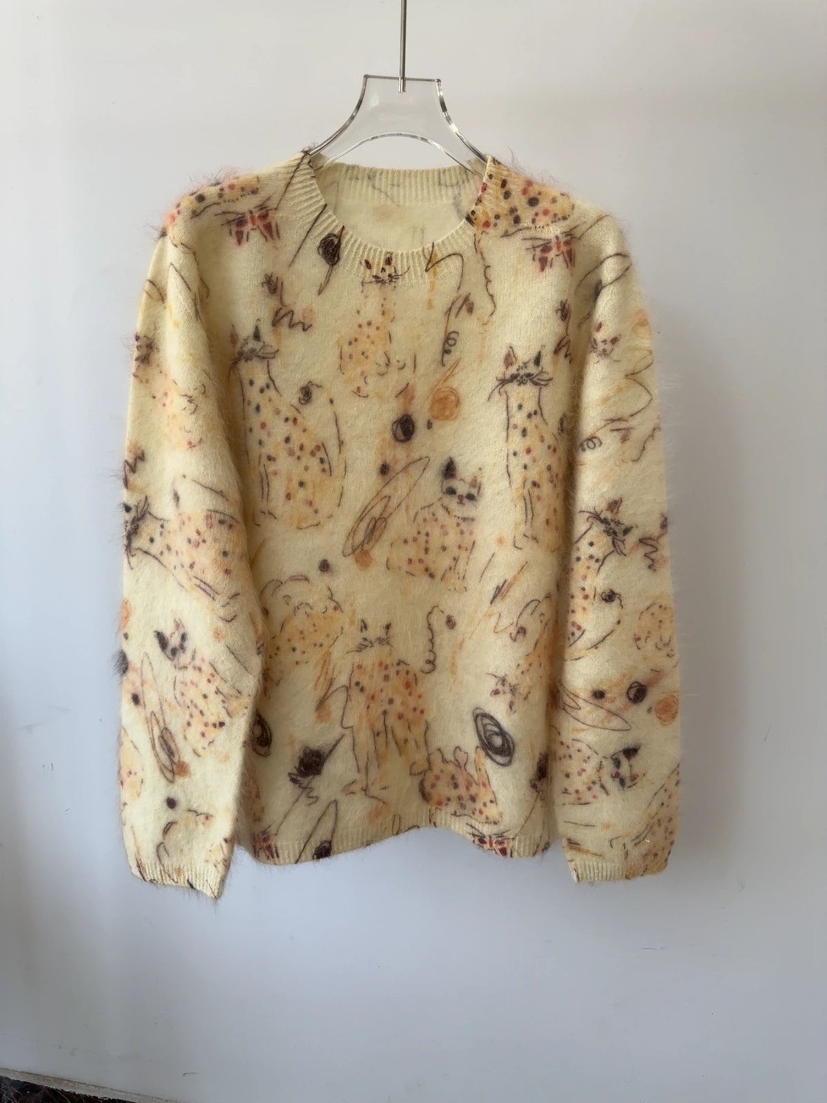 Geborstelde trui met krabbelprint in bruine tinten op een lichtgele basis, hangend aan een hanger
