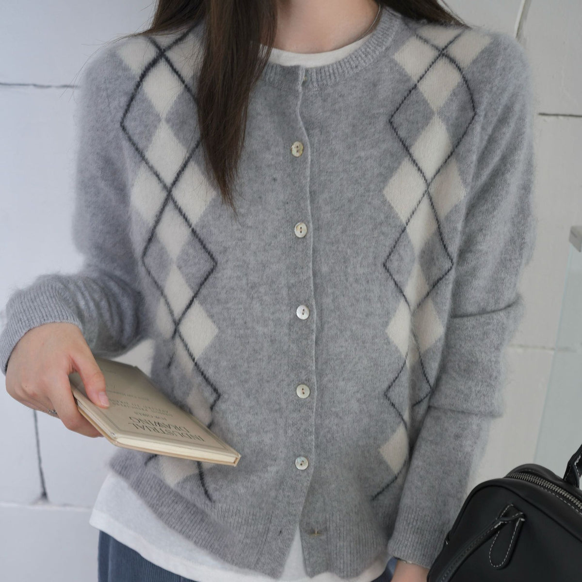 Close-up van lichtgrijs vest met gebroken witte argyle ruiten, met een klein boekje in de hand