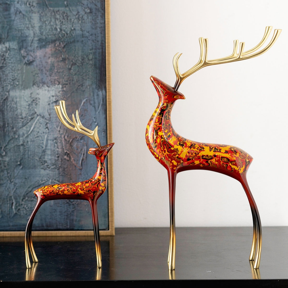Lacquered metal deer figurine with gold-tone antlers, red and orange marbled pattern, standing side view on dark surface