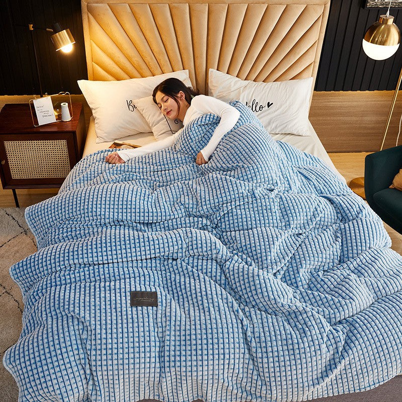Waffle-knit coral fleece throw blanket in sky blue, draped over a person sleeping on a bed with white pillows and a wooden