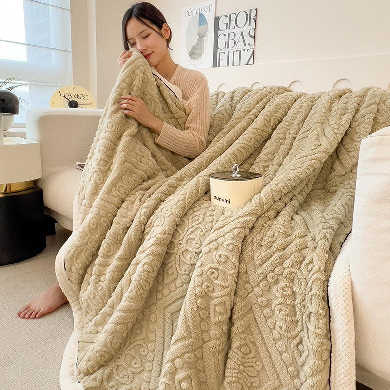 Embossed diamond-pattern velvet-look blanket in beige, partially folded on a sofa, person holding edge, showing pattern and