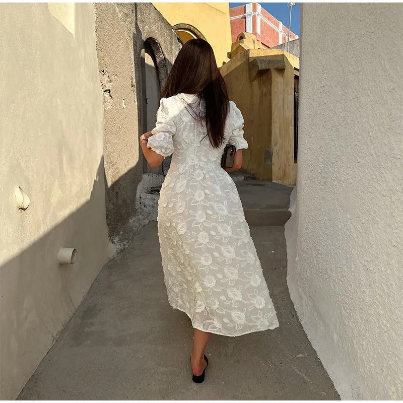 Back view of white embroidered puff-sleeve dress with button front, worn by a model walking through a narrow alleyway