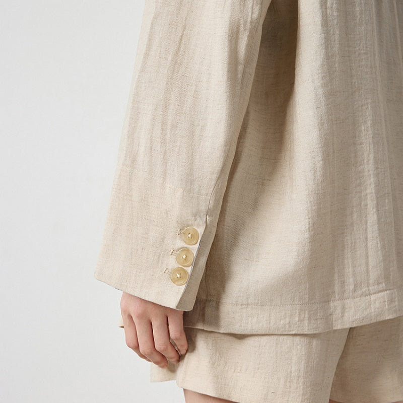 Close-up of beige loose-fit linen-look blazer sleeve showing three gold-tone buttons and striped lining at cuff