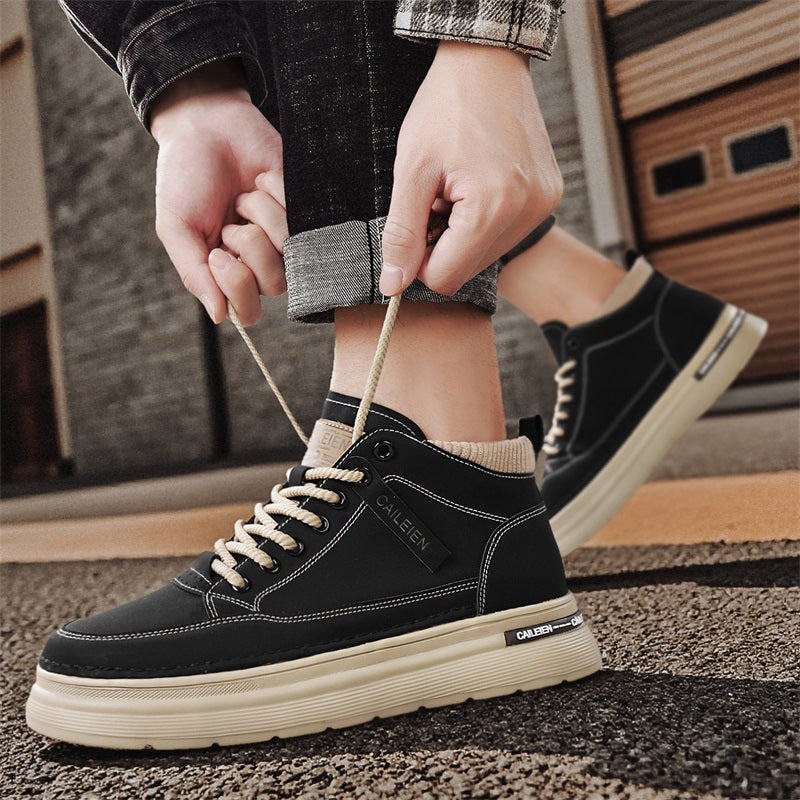 Men's high-top lace-up sneaker boots in black, worn on feet, hands tying laces, urban pavement background
