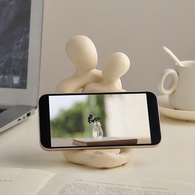 Milky white decorative figurine of an abstract couple holding a phone in its cut-out base, on a desk