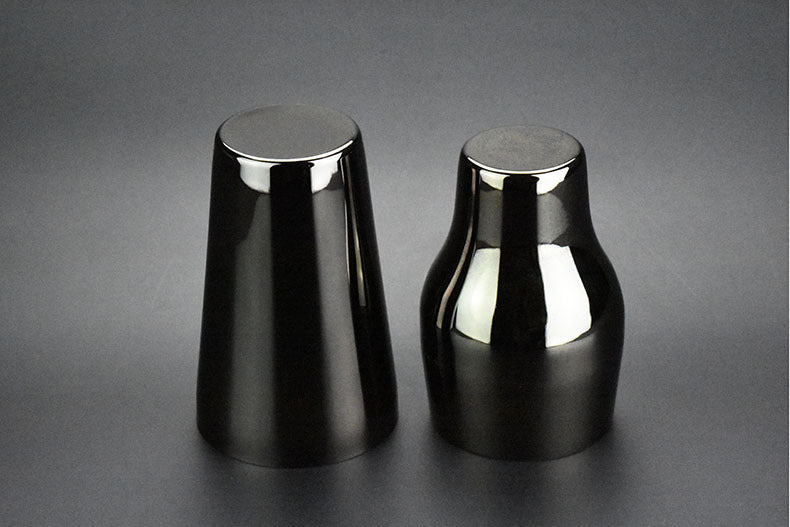 Two-section stainless steel cocktail shaker, 650 ml, black finish, one upright and one inverted, side view, flat lay on dark