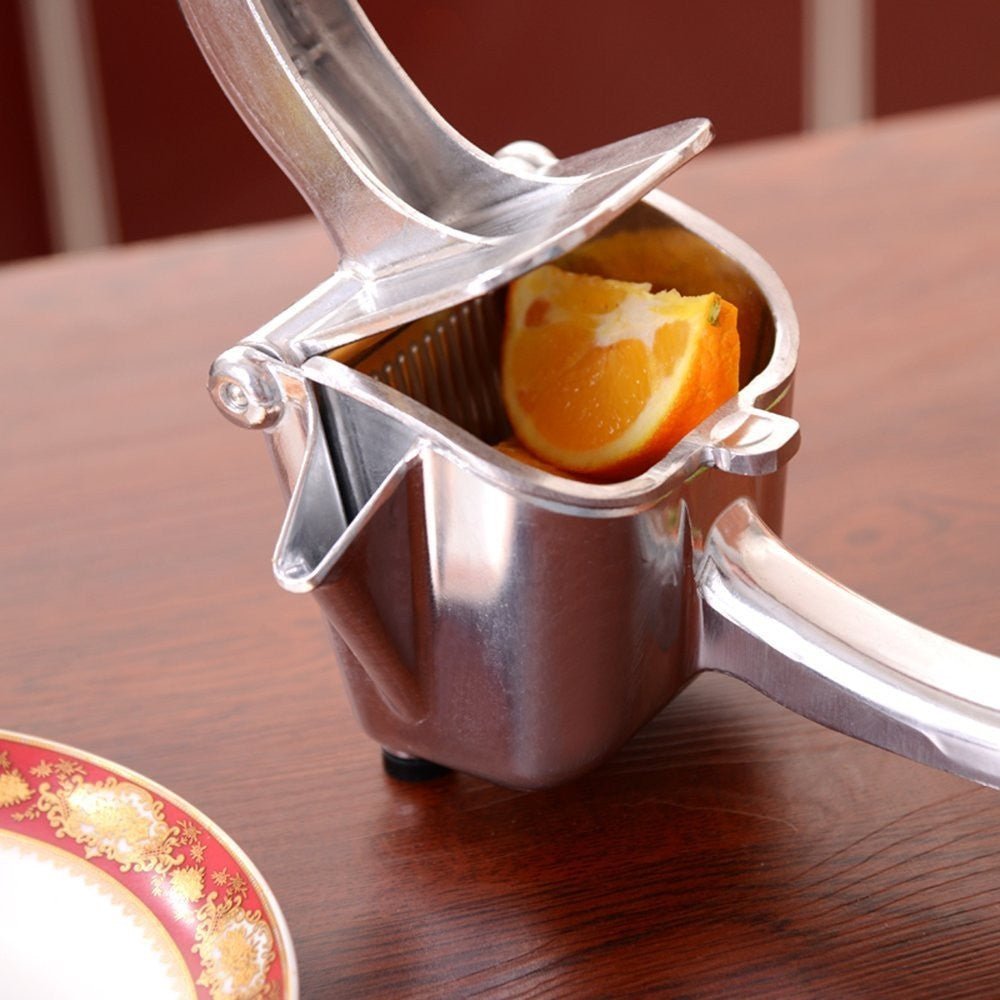 Aluminium hand-lever citrus press with orange slice inside, on wooden table