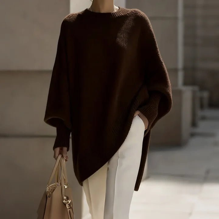 Coffee brown poncho sweater over cream trousers, tan bag in hand