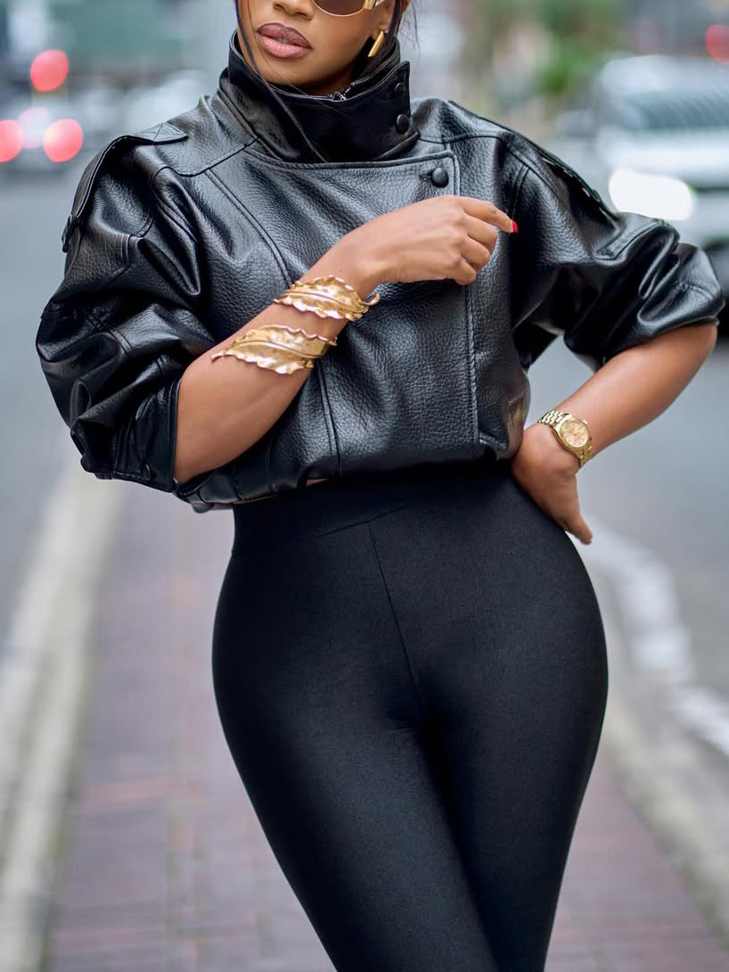 Black faux-leather cropped jacket with puff sleeves, stand collar, worn by model, hand adjusting collar, close-up front view