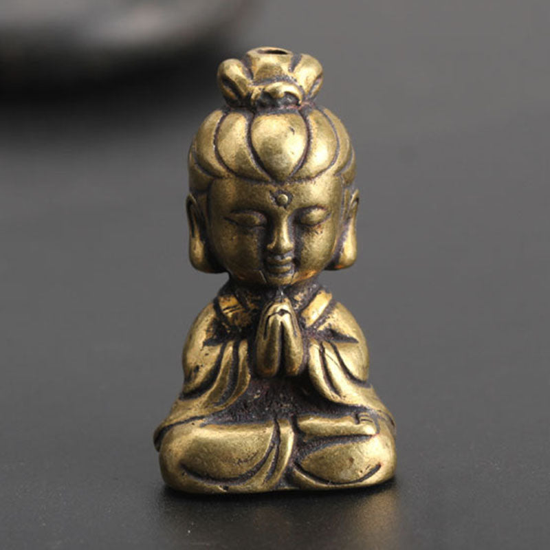 Small brass-look meditating figure ornament, front view, seated with praying hands and topknot, on dark surface
