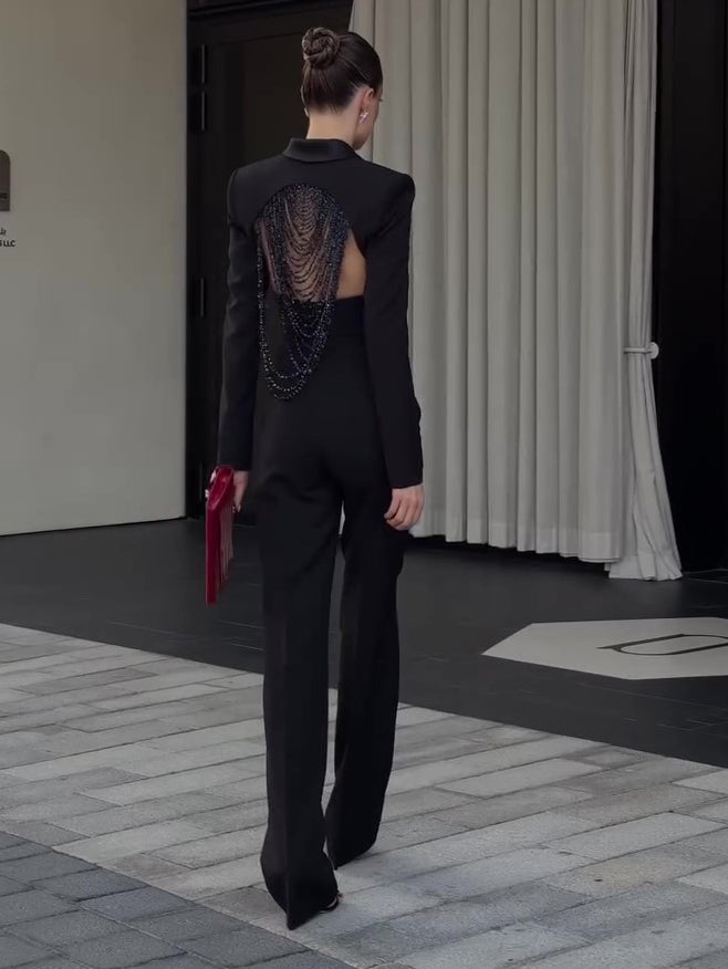 Woman walking away in the black suit, the open back of the cropped blazer filled with bead strands