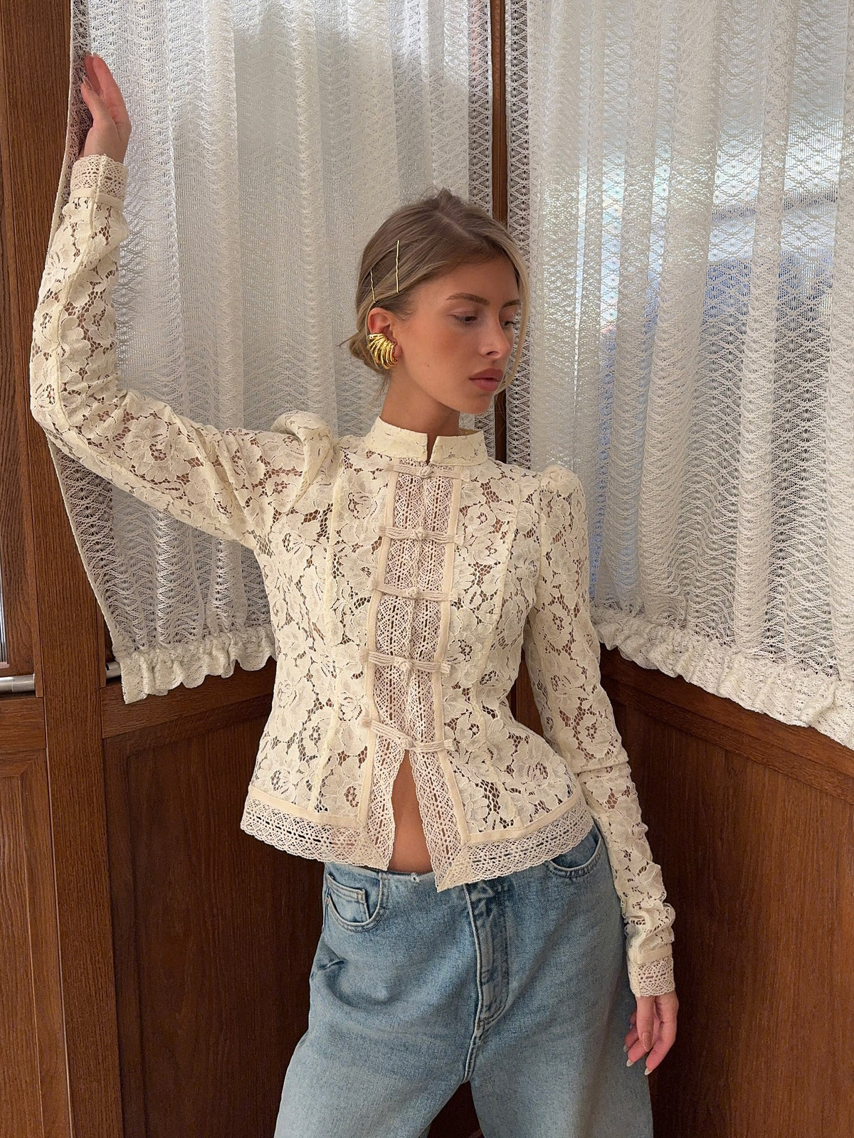 Front view of lace-panel long sleeve blouse with puffed shoulders, cream floral lace, stand collar, on model with jeans