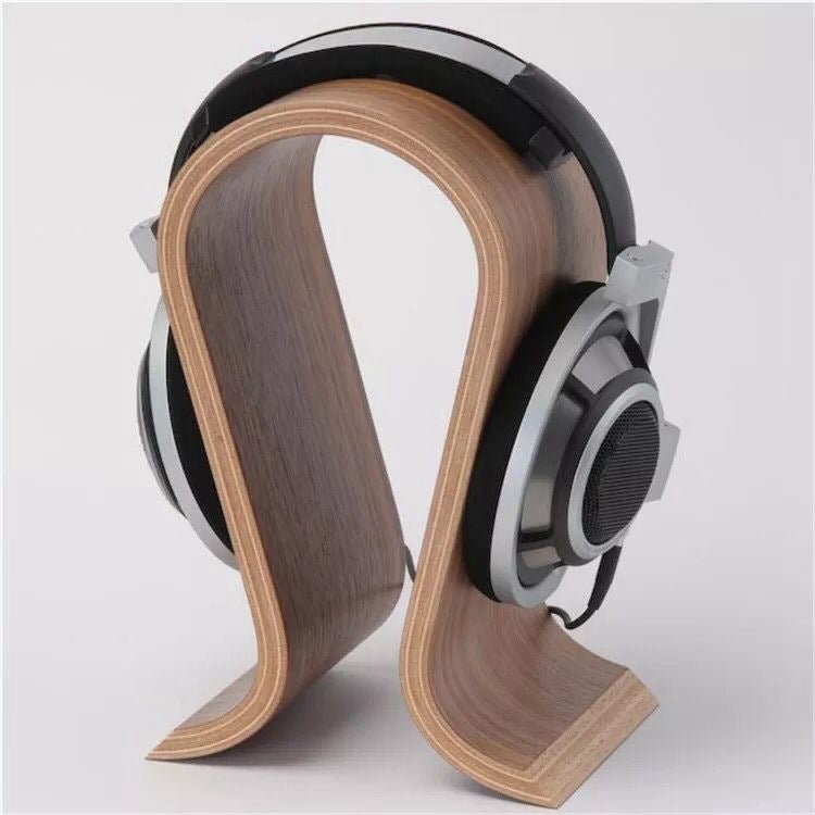 Walnut-coloured bent wood headphone stand in an omega shape with over-ear headphones hanging on it