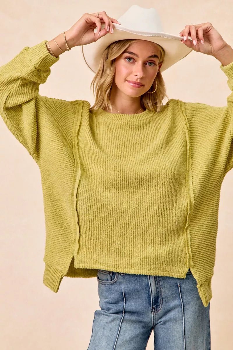 Model wearing BiBi boucle rib knit uneven hem sweater with open seam detail in charcoal grey on light background
